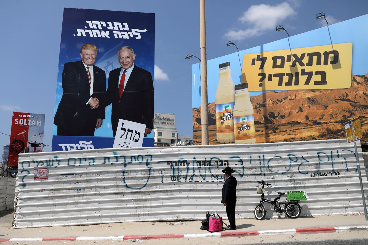 Een ultra-orthodoxe joodse man staat voor een verkiezingsposter van zittend premier Netanyahu, poserend met zijn Amerikaanse politieke vriend Trump. Op de slogan in het Hebreeuws staat vrij vertaald ‘Netanyahu, een ander niveau’.