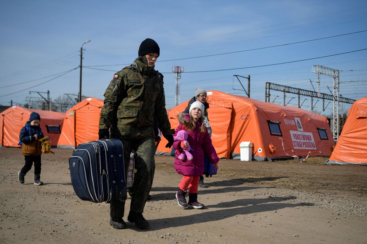Een Poolse militair helpt een Oekraïense familie die op de vlucht is op weg naar de trein.