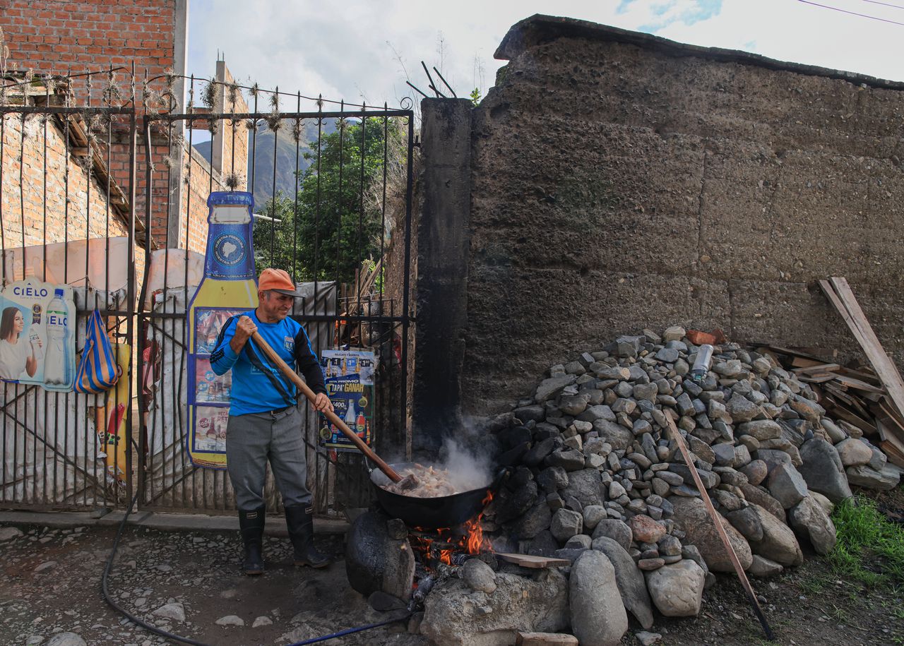 Een man bereidt varkensvlees in een houtgestookte pot buiten zijn huis in Vilcabamba