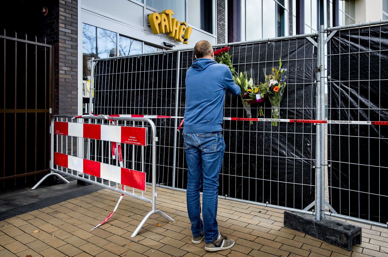 Een man plaatst bloemen tussen de afzettingen bij de Groningse bioscoop waar zaterdag een echtpaar werd gedood.