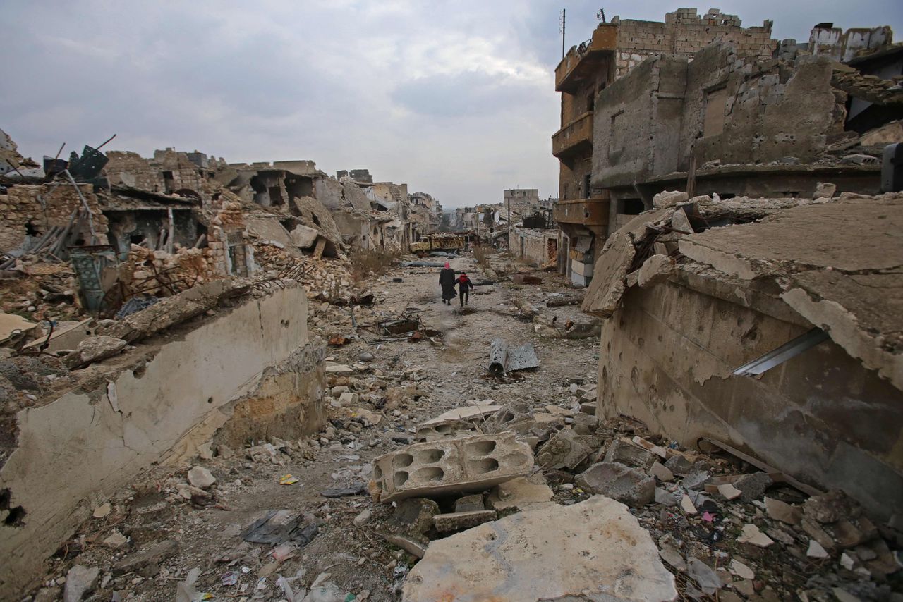 Syriërs lopen in een verwoeste straat in de wijk al-Arkoub, in Aleppo eind 2016.
