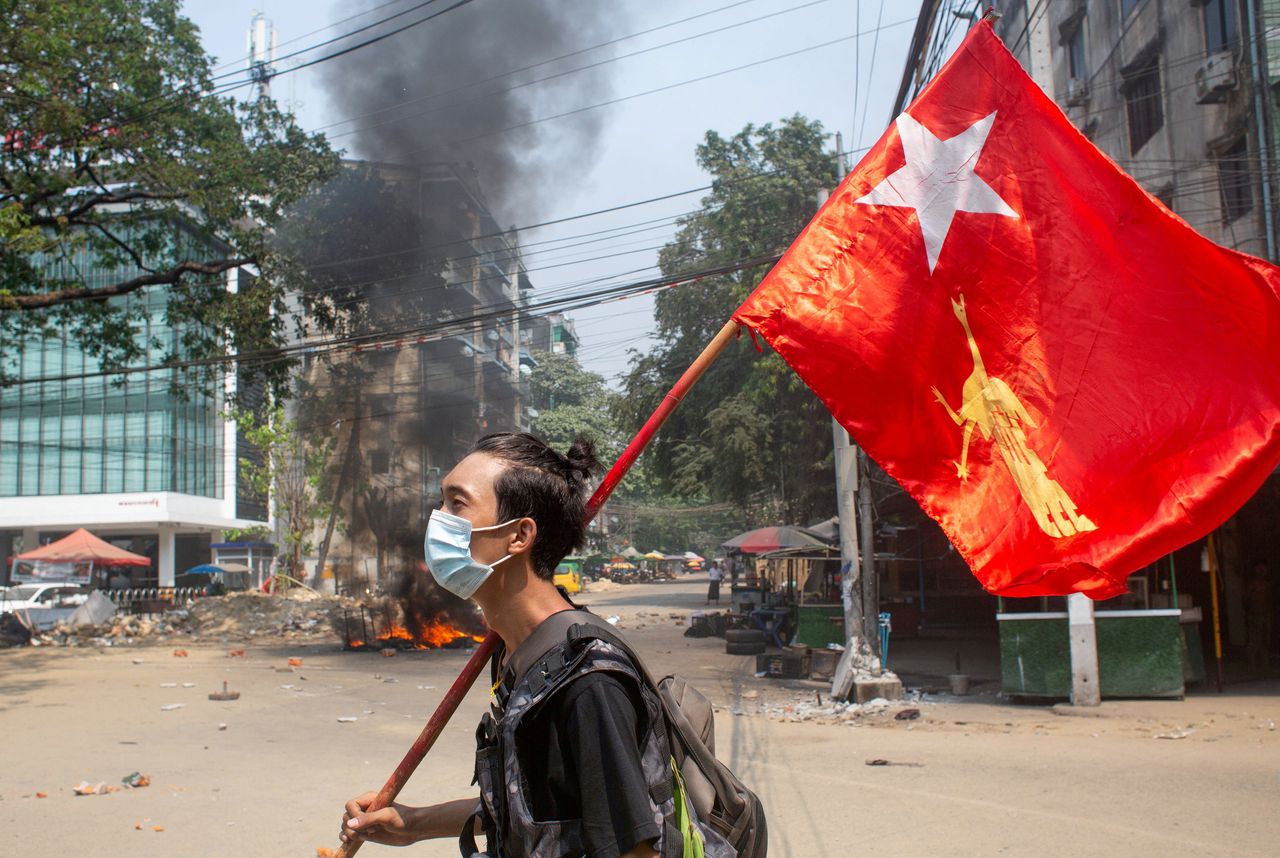 Een man protesteert in Myanmar tegen de militaire coup. In zijn hand draagt hij een vlag van de Nationale Liga voor Democratie (NLD).