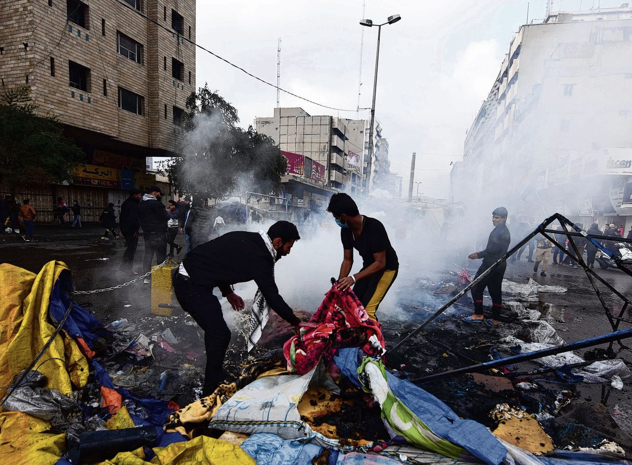 Iraakse betogers ruimen puin nadat hun tentenkamp op en rond het Tahrir-plein door de politie in brand is gestoken.