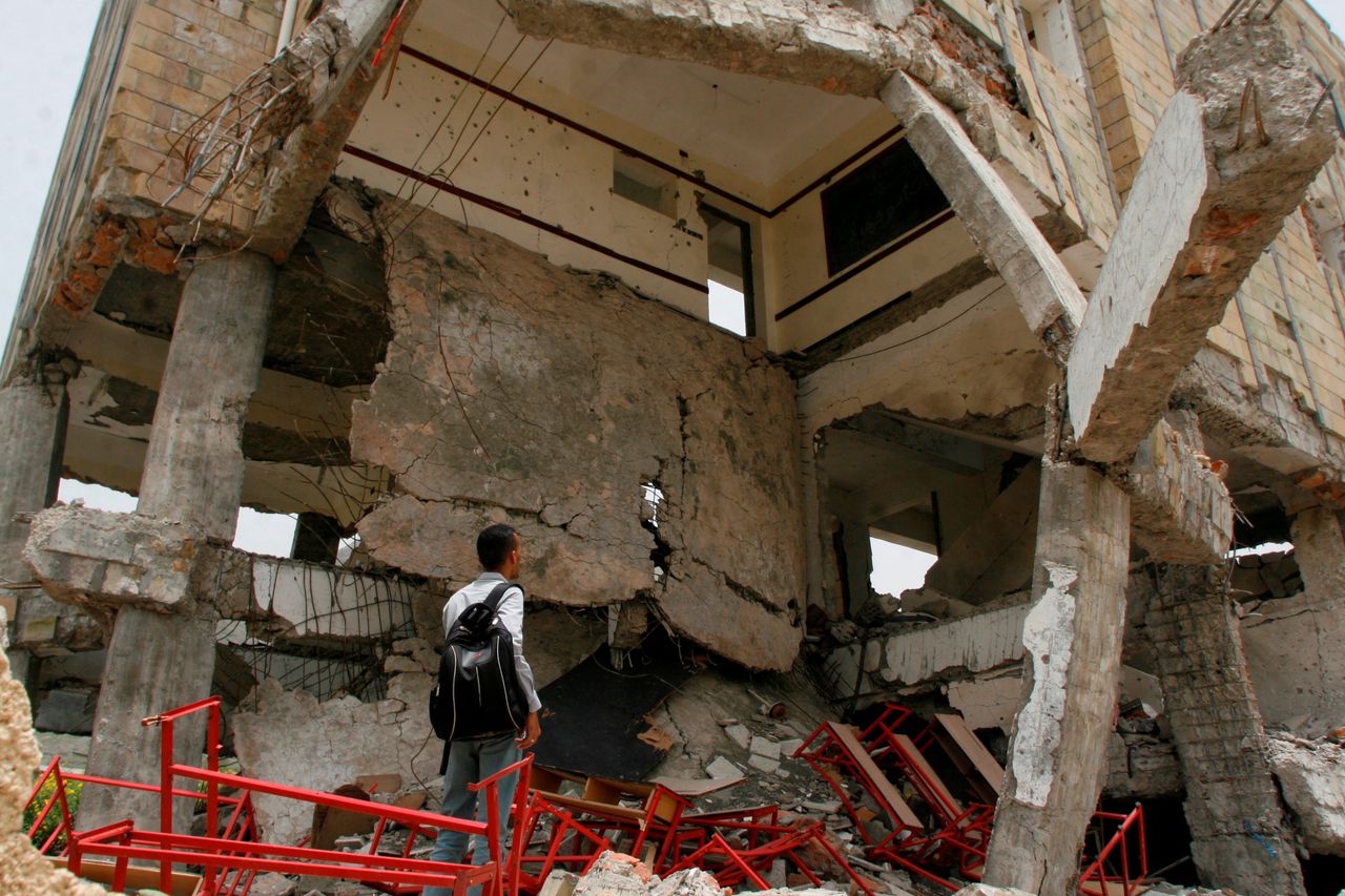 Een man kijkt naar een gebouw dat gebombardeerd is door de internationale coalitie onder leiding van Saoedi-Arabië.