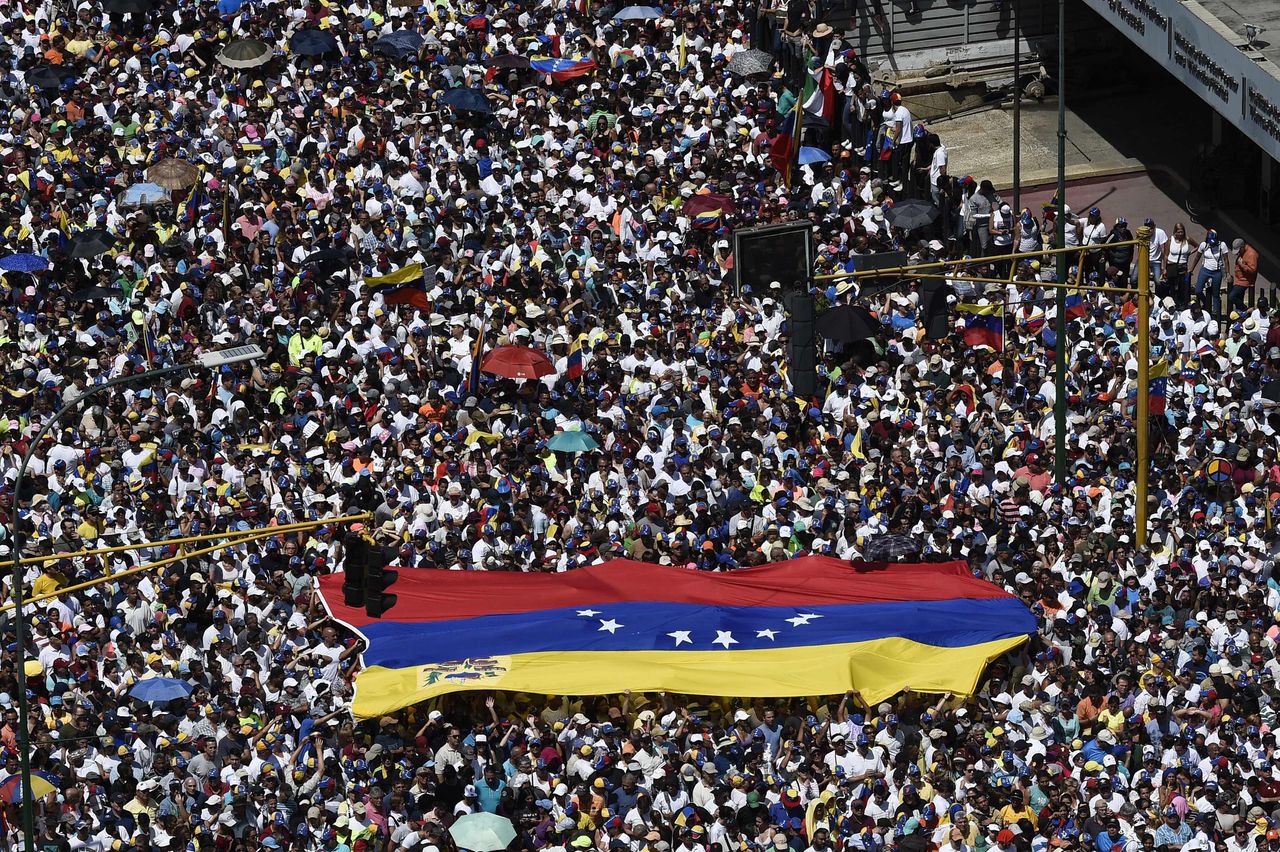 Aanhangers van Guaidó dragen zaterdag een grote Venezolaanse vlag door de straten van Caracas.