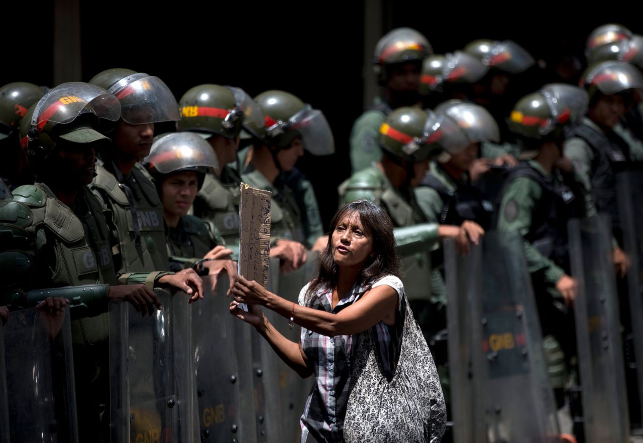 Een Venezolaanse vrouw loopt met een protestbord langs leden van de Nationale Garde, deze maand in Caracas.