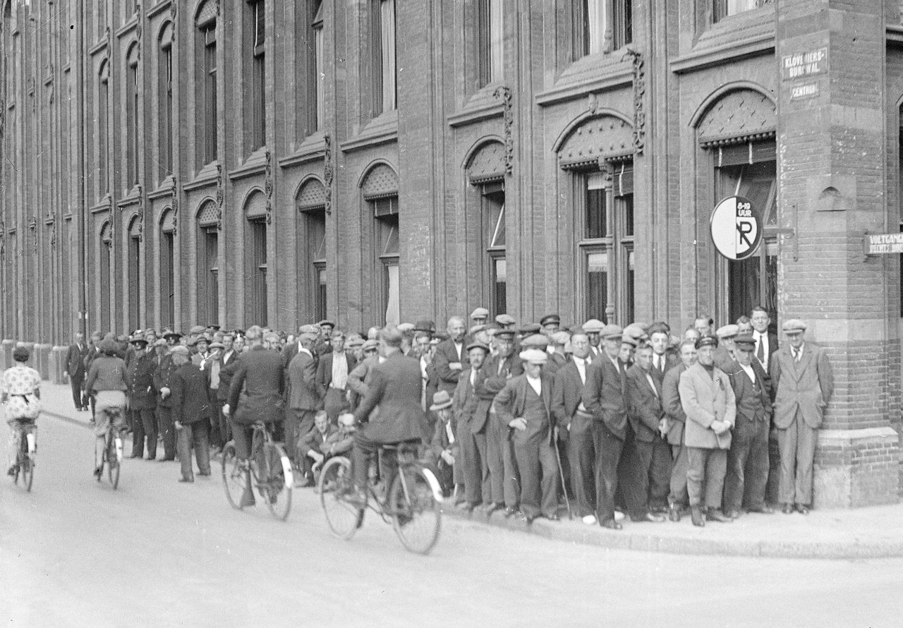 Lange rijen wachtenden op de Kloveniersburgwal in Amsterdam om om de hoek ieen gratis rijwielplaatje te krijgen. Deze maatregel werd in de jaren dertig ingevoerd vanwege de economische crisis.