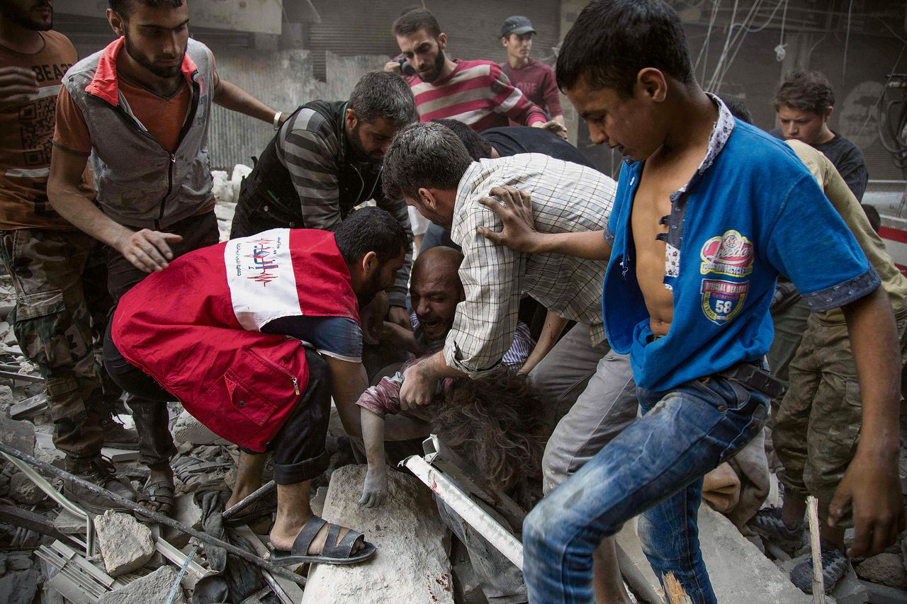 Omstanders omringen een man wiens dochtertje net levenloos onder het puin vandaan is gehaald, in Aleppo.