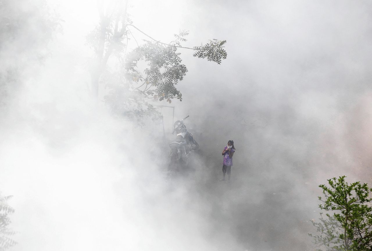 Een Indiaas meisje gehuld in rook, nadat de autoriteiten van de stad Ahmedabad met een desinfecterend middel een woonwijk proberen te ontsmetten.