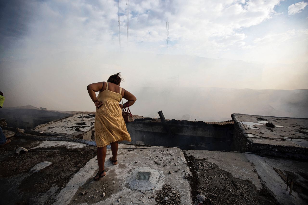 Een Haïtiaanse vrouw kijkt neer op een uitgebrande marktplaats.