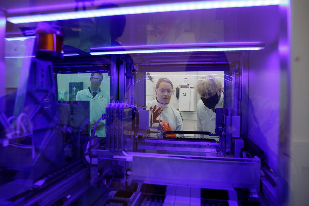 De Britse premier Boris Johnson bekijkt een machine waarmee in monsters het coronavirus kan worden opgespoord.