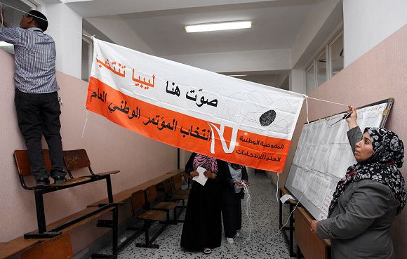 Caption: Libyan polling station workers raise a banner at a school turned polling station in the Tajura district of Tripoli on July 6, 2012 on the eve of a general election. Libya will hold landmark elections for a national assembly, the first democratic poll after more than four decades of dictatorship under Moamer Kadhafi, who was toppled and killed last year. AFP PHOTO/MAHMUD TURKIA