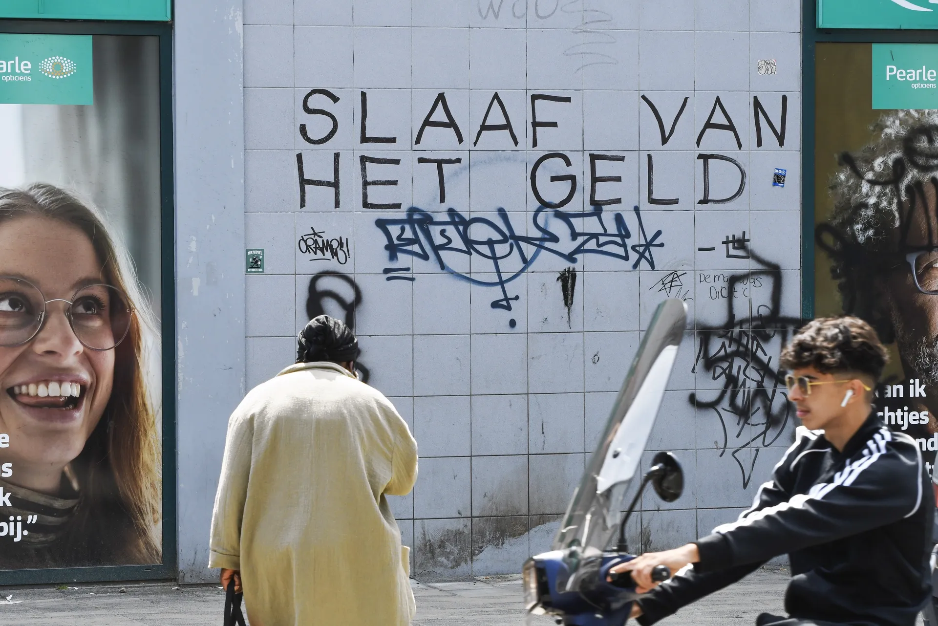 Foto van straat met slogan op muur: ‘Slaaf van het geld’