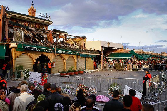 A crowd congregates outside the Argana Marrakech cafe where a terrorist set off a nail-packed bomb, killing at least 16 people in the Morocco's tourist city, Sunday, May 1, 2011. Flower tributes lay outside a cordon off building as polices officers stands to keep eyes on. (AP Photo/Abdeljalil Bounhar)