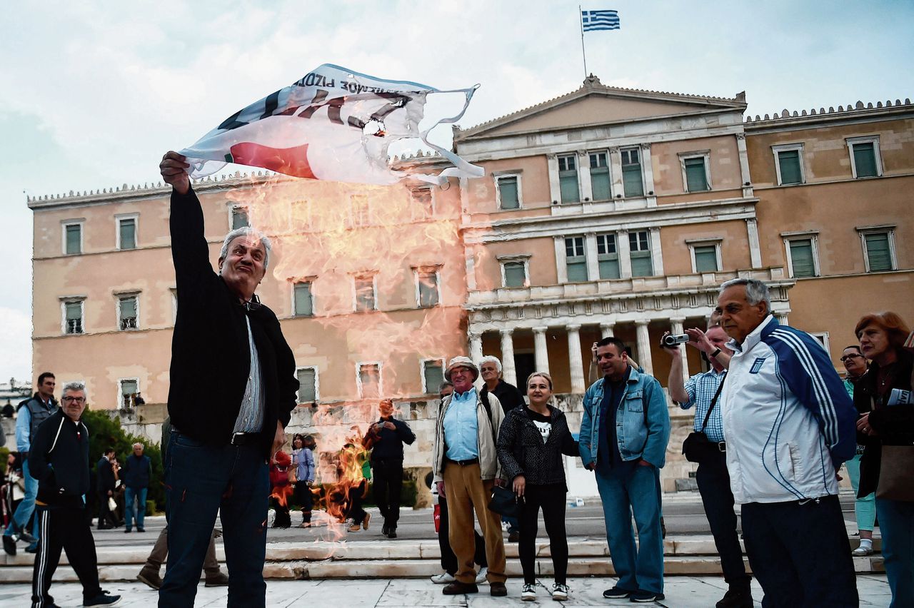 Buiten het Griekse parlement verbrandt een betoger een Syriza-vlag als protest tegen nieuwe bezuinigingen.