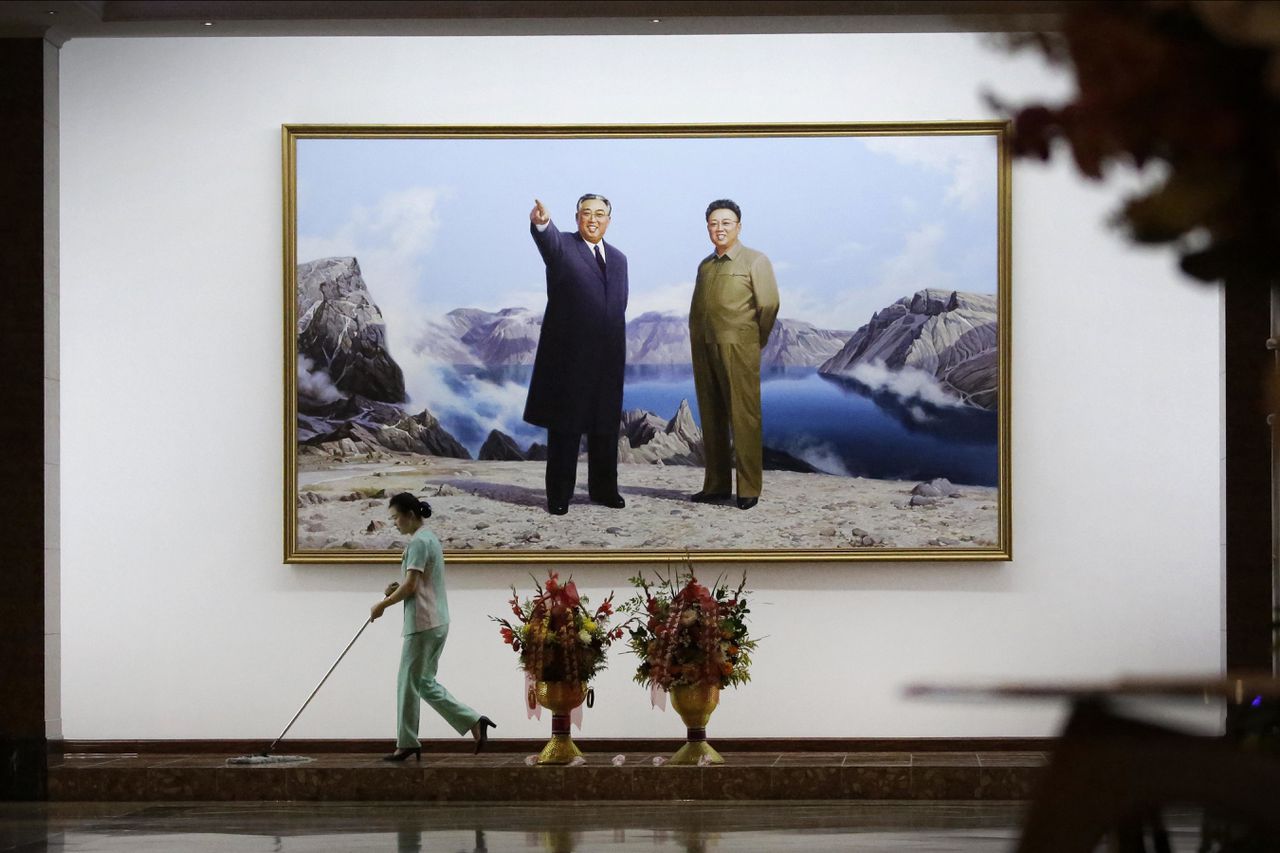 Een hotelmedewerker maakt de vloer schoon bij een portret van de Noord-Koreaanse leiders Kim Il Sung (l) en Kim Jong Il.