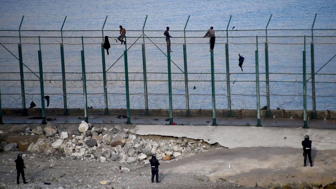 Enkelen van de migranten die vrijdagochtend urenlang in het zes meter hoge hek op de grens met Ceuta zaten, gezien vanaf de Spaanse zijde.