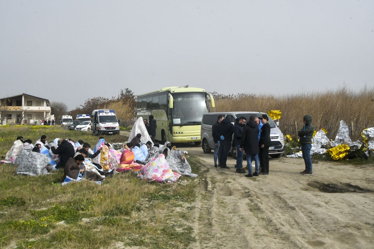 Geredde migranten worden warmgehouden met dekens op het strand in het zuiden van Italië.