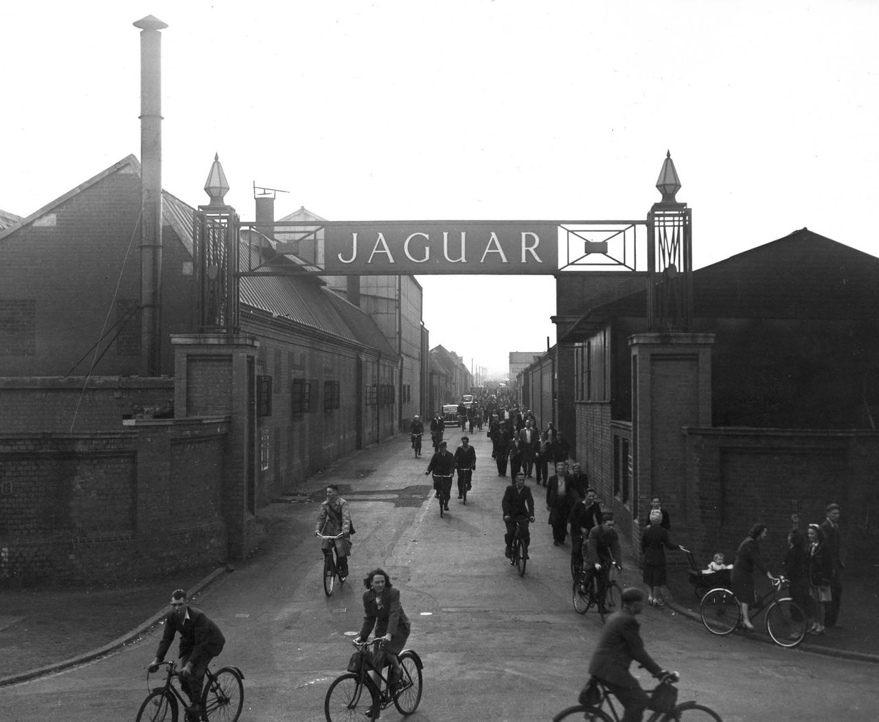 Arbeiders verlaten de Jaguar-fabriek in het Britse Coventry, rond 1936. Foto Bloomberg Workers exit the Jaguar manufacturing facility in Coventry, England in this circa 1936 company photograph. Now that Ford Motor Co. has slashed overhead by deciding to close a Jaguar factory in England, an even more daunting task lies ahead: figuring out what future Jaguars will look like. Source: Wieck/Via Bloomberg News.