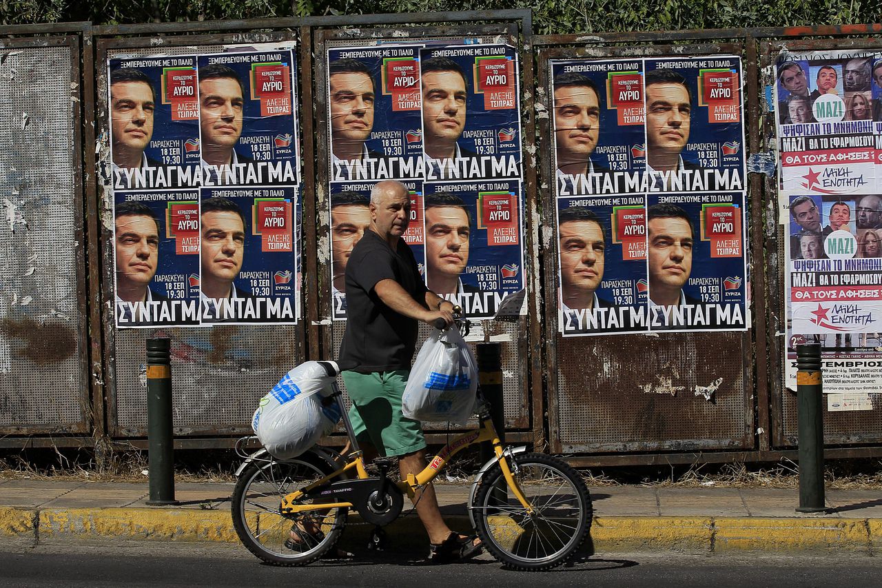 Een Griekse man loopt langs een aanplakbord met daarop het gelaat van Syriza-leider Tsipras.