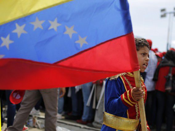 A boy dressed as a soldier from colonial period carries the national flag in a crowd of supporters of Venezuela's late President Hugo Chavez at the Military Academy in Caracas, March 7, 2013. Venezuelans flocked to pay tribute to Chavez two days after he died of cancer. REUTERS/Tomas Bravo (VENEZUELA - Tags: POLITICS OBITUARY)