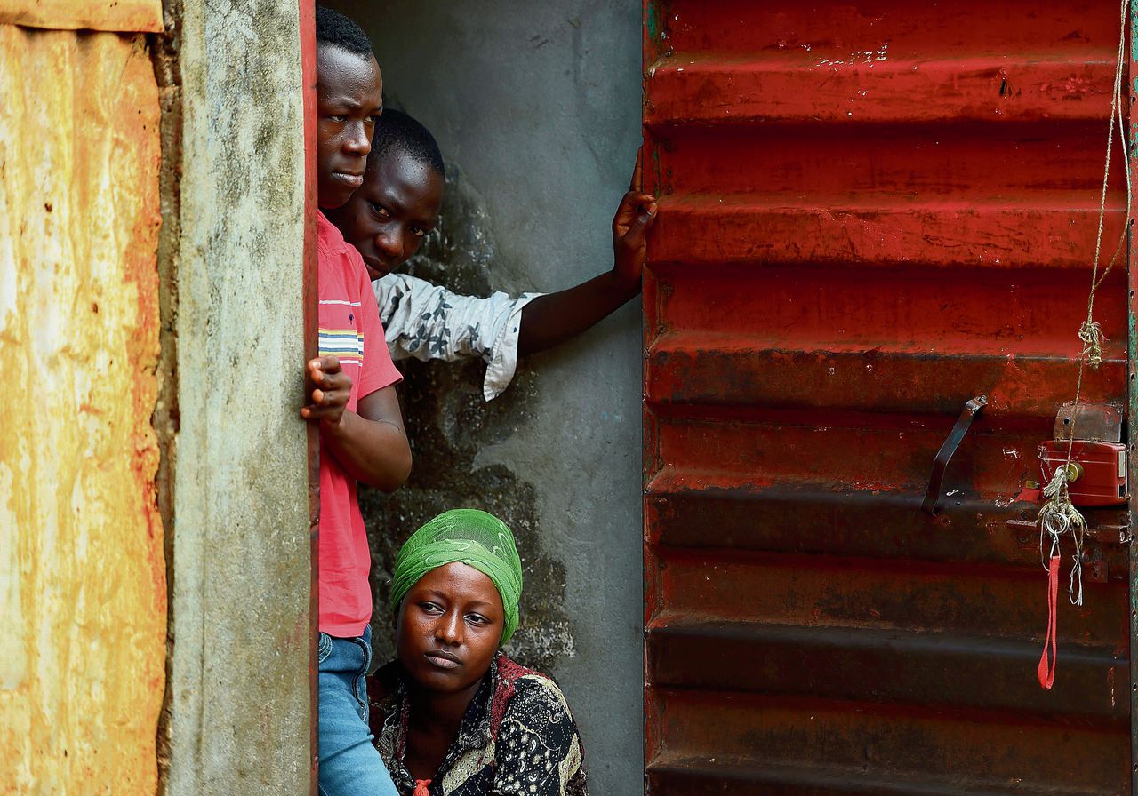Een familie gluurt naar binnen bij een huis dat in quarantaine is in verband met ebola in Freetown. Foto AFP/FRANCISCO LEONG