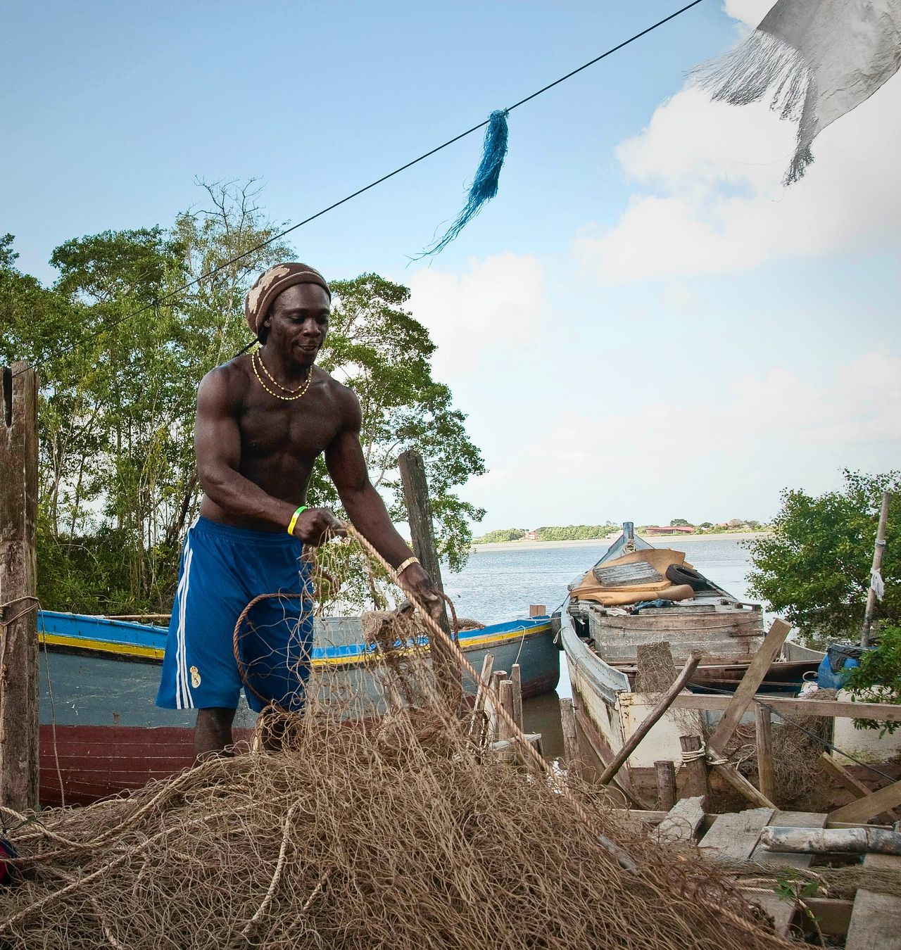 Suriname, Commewijnedistrict, Marron visser bezig met het ordenen van de netten bij de vissersbootjes aan de rivier.