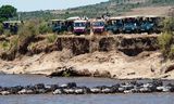 Toeristen staan op de uitkijk bij de door de aanwezigheid van krokodillen gevaarlijke oversteek van gnoes door de Mara-rivier in het Keniaanse wildreservaat Maasai Mara.