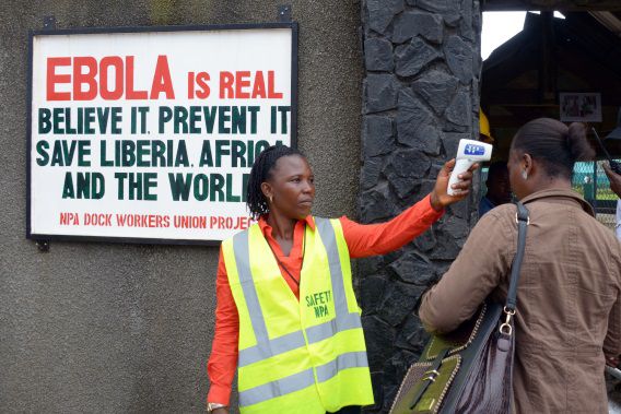 Een veiligheidsmedewerker controleert de lichaamstemperatuur van passanten bij de haven van Monrovia.