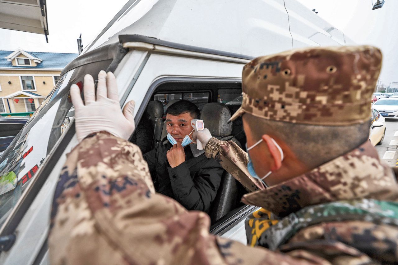 Een militair controleert de lichaamstemperatuur van een automobilist in Wuhan, om vast te stellen of hij niet besmet is met het coronavirus.