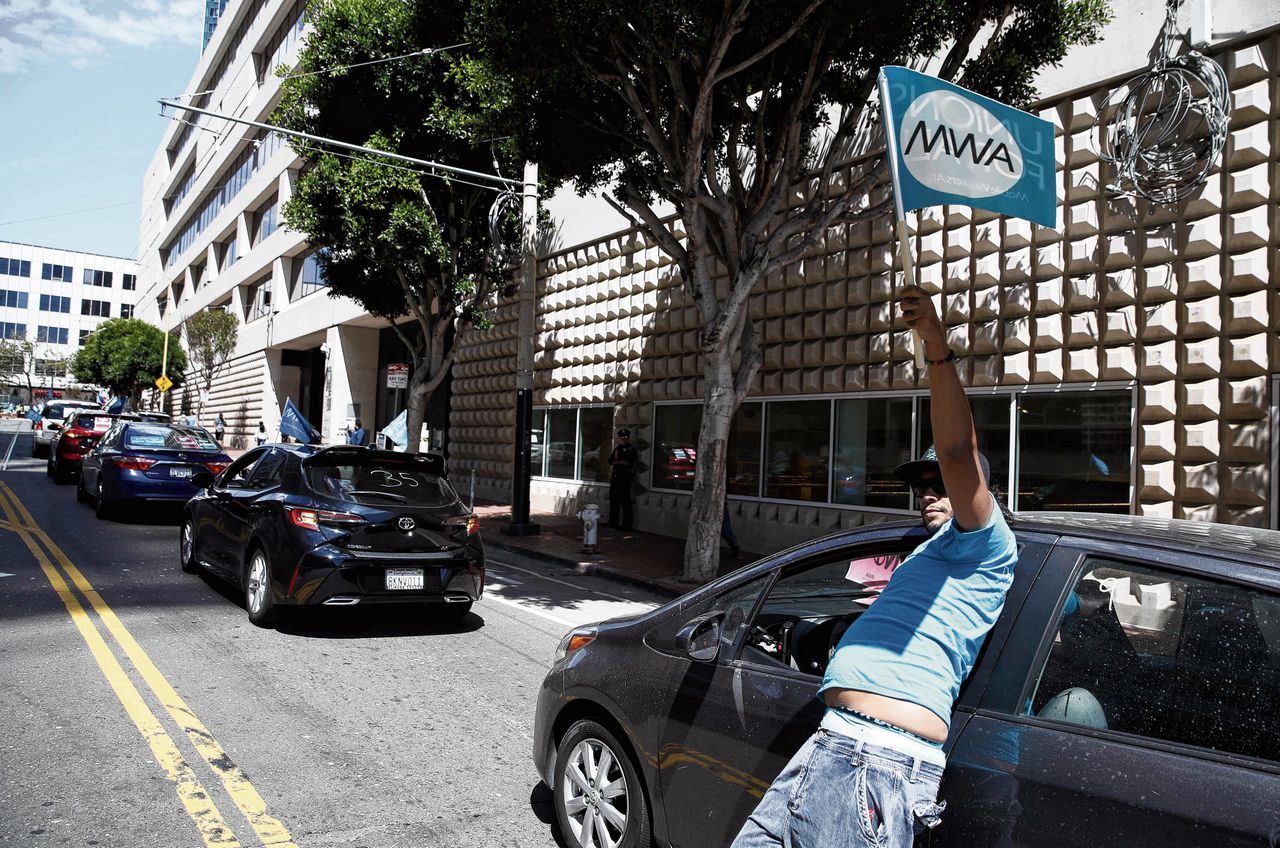 Een taxichauffeur in San Francisco zwaait met een vakbondsvlag om te vieren dat Uber door een nieuwe arbeidswet in Californië freelance chauffeurs vanaf 2020 vast in dienst moet nemen.