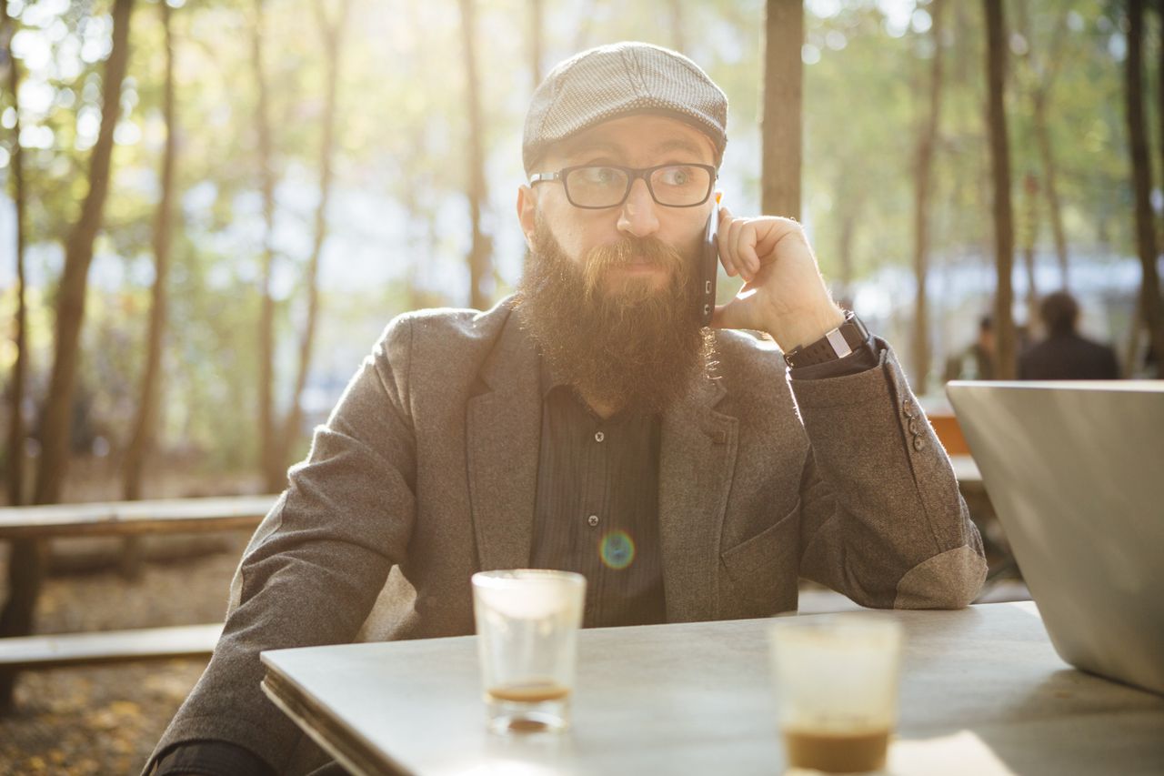 04 Oct 2014, Berlin, Germany --- Germany, Berlin, beared man sitting in a garden cafe using smartphone --- Image by © fotografixx/Westend61/Corbis