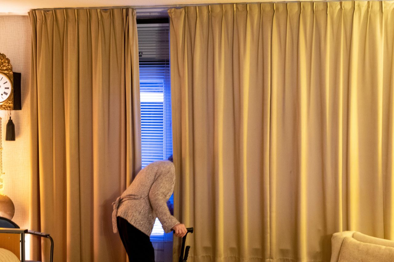 Fotograaf Hans van Rhoon fotografeert zijn dementerende moeder van 97 jaar als ze de gordijnen dicht doet voor de nacht. Haar bed staat in de huiskamer.