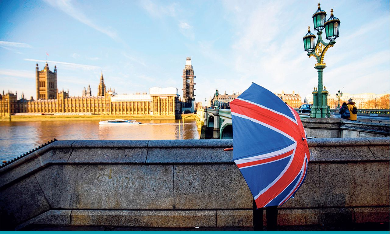 Een kraamhouder van een souvenirstalletje opent een paraplu met de Britse vlag tegenover het parlementsgebouw in Londen