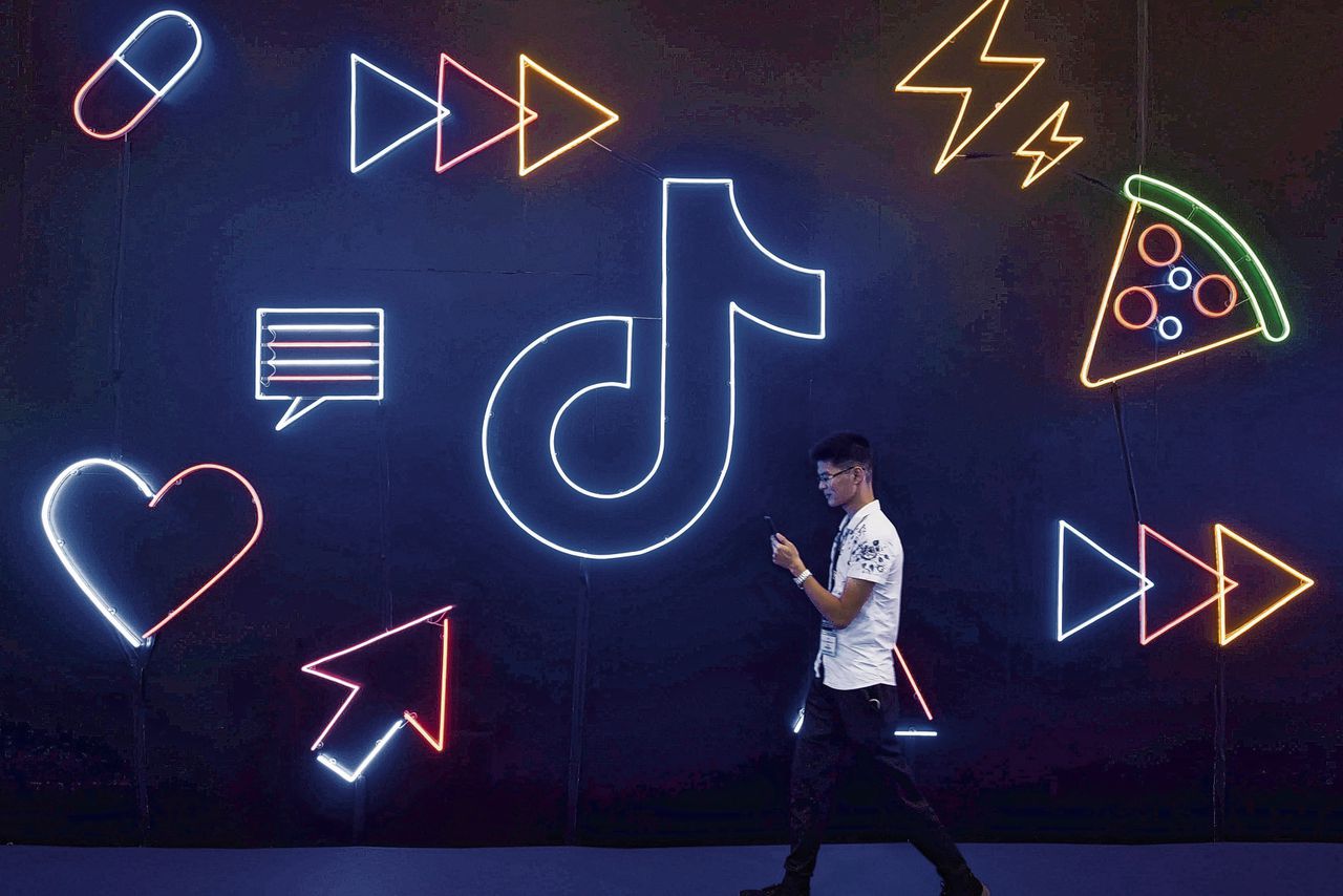 A man holding a phone walks past a sign of Chinese company ByteDance's app TikTok,