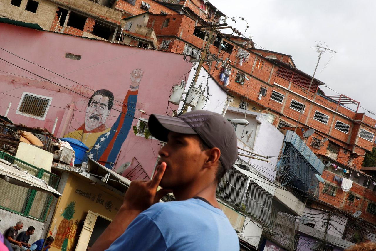 Een bewoner wacht op de bus in de wijk José Félix Ribas in de hoofdstad van de Venelozaanse hoofdstad Caracas. Achter hem is een muurschildering van president Maduro te zien. Ook zijn arme achterban, in sloppenwijken zoals deze, keert zich nu meer van hem af.