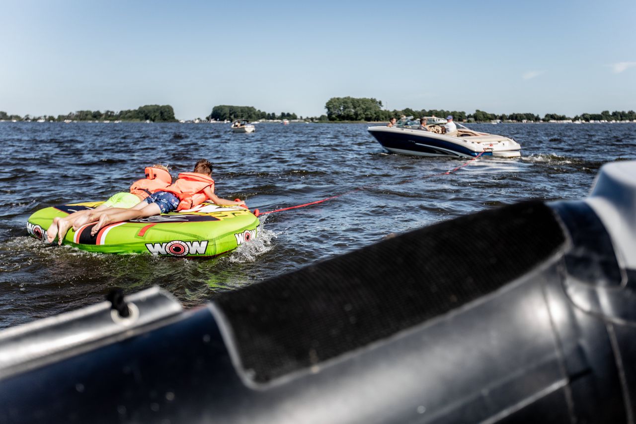 Twee kinderen op een opblaasbare tube op het Sneekermeer worden getrokken door een motorboot.