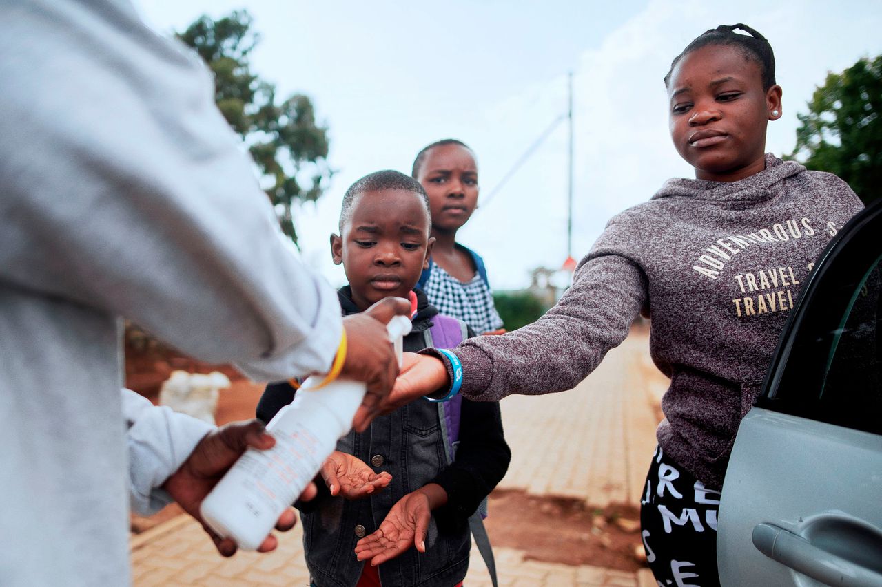 Medewerkers van het Rode Kruis geven desinfecterende gel aan bewoners in een buitenwijk ten westen van Soweto.