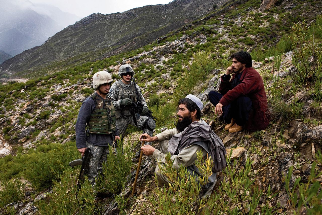 Een Afghaanse tolk (links) vertaalt vragen van een Amerikaanse soldaat (tweede van links) aan twee mannen in oostelijk Afghanistan in april 2009.