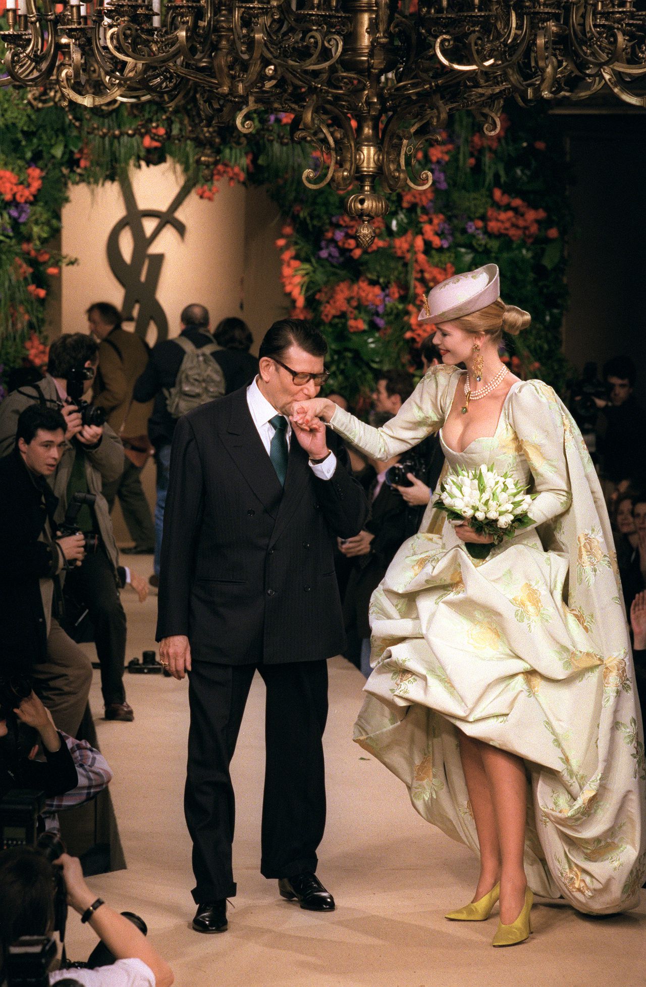 Yves Saint Laurent en model Claudia Schiffer bij een modeshow in 1997. Foto AFP (FILES) French designer Yves Saint Laurent hand kisses model Claudia Schiffer, on January 22 1997 in Paris, after the presentation of his Spring-summer Haute Couture collection. Yves Saint Laurent, one the top French designers of the 20th century, died in the evening on June 01, 2008, in Paris, the Pierre-Berge-Saint Laurent Foundation said. The reclusive French maestro, who had retired from haute couture in 2002 after four decades at the top of his trade, had been ill for some time. AFP PHOTO PIERRE VERDY