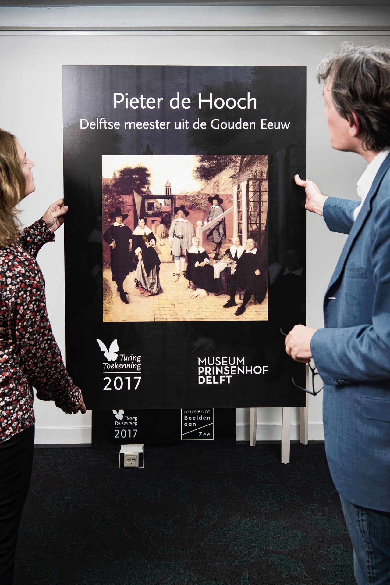 Françoise en Pieter Geelen wilden niet herkenbaar op de foto. Ze staan voor een affiche van de expositie in Delft over Pieter de Hooch, die ze met 500.000 euro steunen.