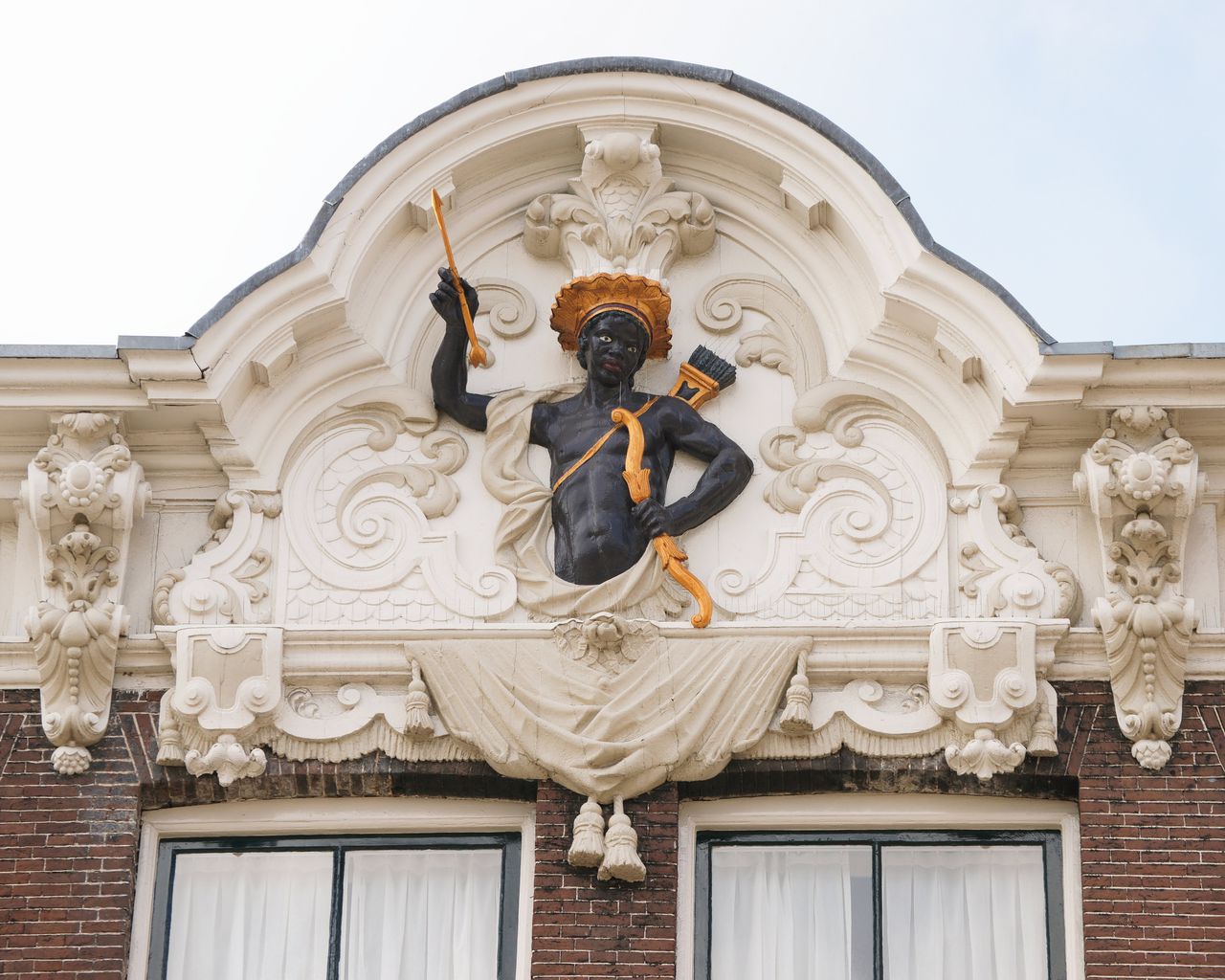 ‘De Moriaan’, gevel Rokin 64, Amsterdam. Een zwarte figuur die met zijn pijlen naar de Amerikaanse inheemsen verwijst. Historisch onderzoek naar de oorsprong van kolonialisme en racisme is onmisbaar voor ons begrip van het verleden.