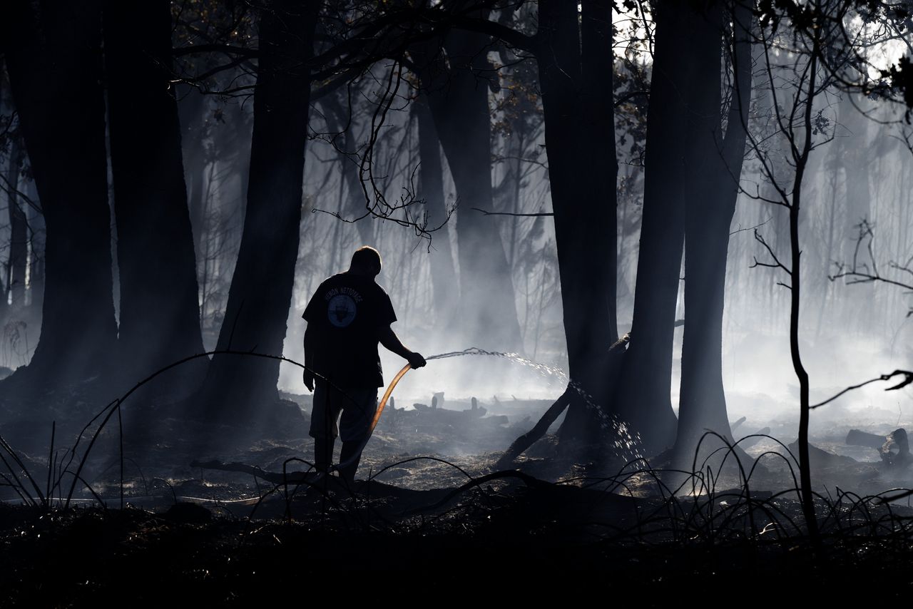 Een man besproeit smeulende bossen in de West-Franse Gironde.