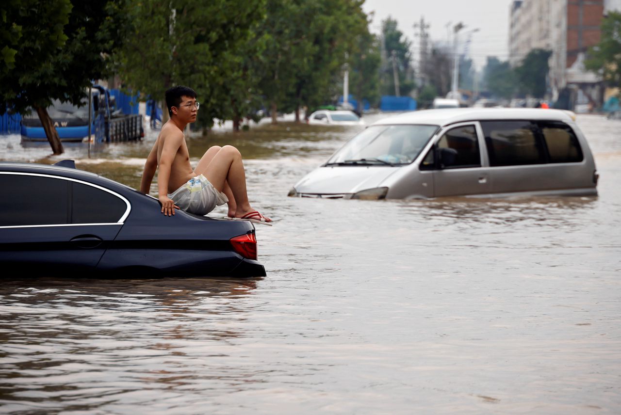 Een man op een auto bij een overstroming eind juli in het Chinese Zhengzhou.
