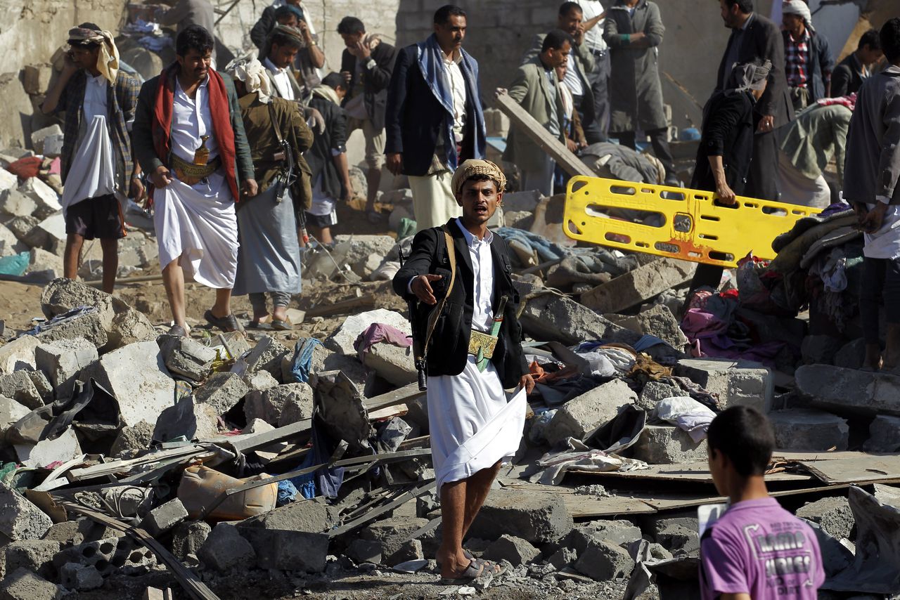 Gewapende Houthi-rebellen te midden van huizen die verwoest zijn door luchtaanvallen.
