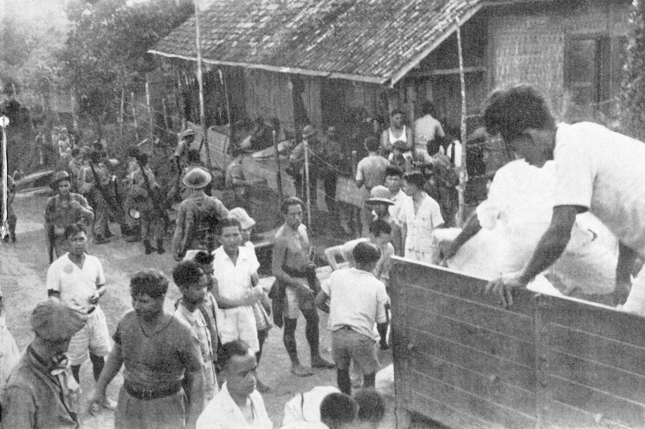 Het uitladen van rijst bij de tangsi van Pempatan, waar een aantal gevangenen vastgebonden in de voorgalerij ligt.