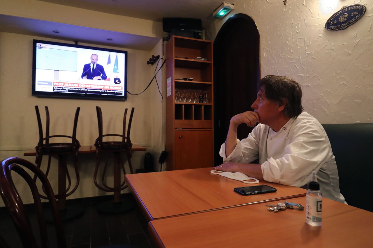 Een Franse restauranthouder kijkt naar de persconferentie waarin de Franse premier aankondigt dat cafés en restaurants weer open mogen.