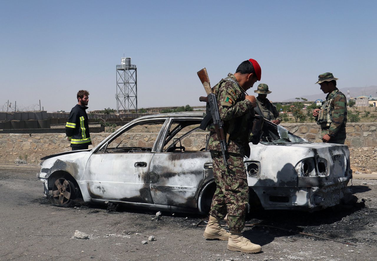 Afghaanse veiligheidstroepen inspecteren een autowrak bij de plek van de aanslag.