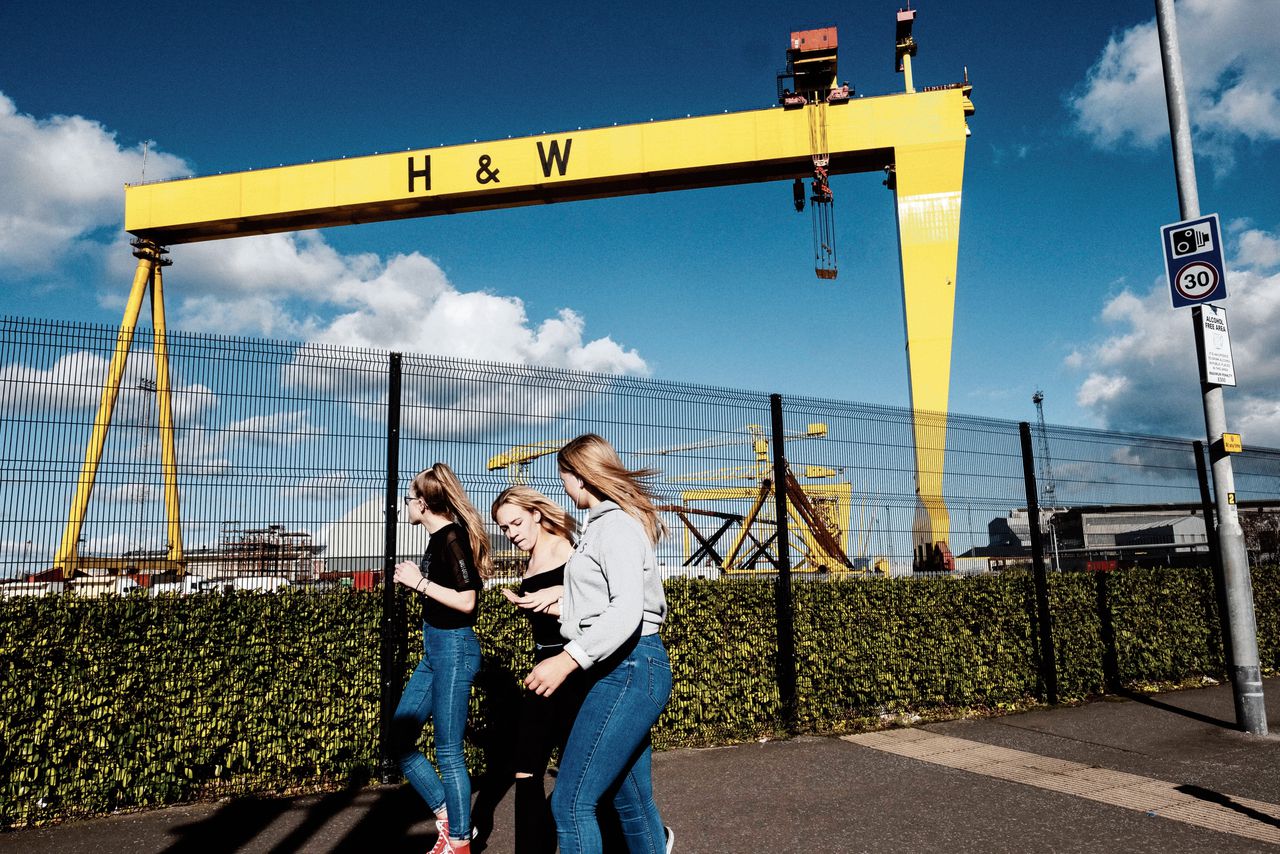 Scholieren lopen in Belfast langs de Harland & Wolff scheepswerf, waar onder andere de Titanic is gebouwd (boven). Rechts straatbeelden uit de Noord-Ierse hoofdstad.