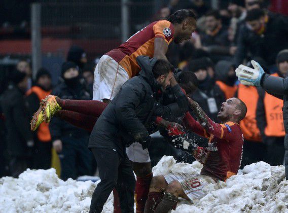 Wesley Sneijder (rechts) ligt in de sneeuw en wordt besprongen door teamgenoot Didier Drogba, nadat hij de winnende goal heeft gemaakt voor Galatasaray tegen Juventus. De Turkse club gaat zodoende door naar de achtste finales van de Champions League.
